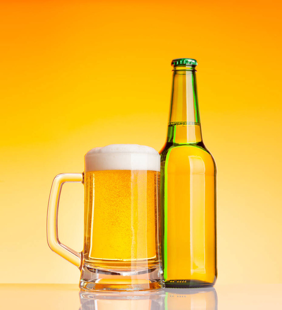 Butelka po piwie i szklanka z piwem przed żółtym tłem. Zdjęcia studyjne - Zdjęcie, obraz