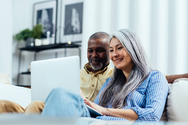 Cinematic image of an happy multiethnic senior couple. Indoors Lifestyle moments at home. Concept about seniority and relationships - Photo, image