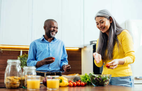cinematic image of a multiethnic senior couple preparing food in the kitchen. Indoors Lifestyle moments at home. Concept about seniority and relationships - Foto, afbeelding