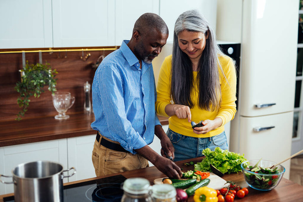 cinematic image of a multiethnic senior couple preparing food in the kitchen. Indoors Lifestyle moments at home. Concept about seniority and relationships - Fotoğraf, Görsel