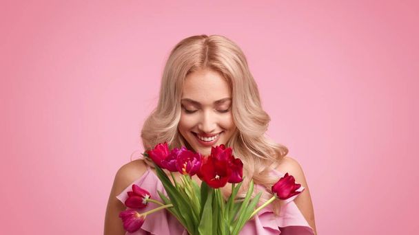 Feliz rubia hembra celebración ramo de tulipanes sobre fondo rosa - Foto, imagen