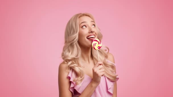 Žena pózování jíst lízátko líbání cukroví mrkání oko, růžové pozadí - Záběry, video