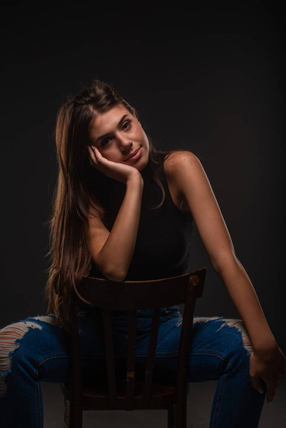 Beautiful and attractive girl is sitting on the chair while posing in studio - Фото, изображение