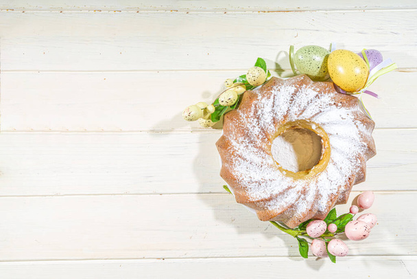 Traditionele voorjaarsvakantie Pasen ronde taart belegd met poedersuiker. Op lichte houten ondergrond met zonlicht, paaseieren, decor en lentetakken - Foto, afbeelding