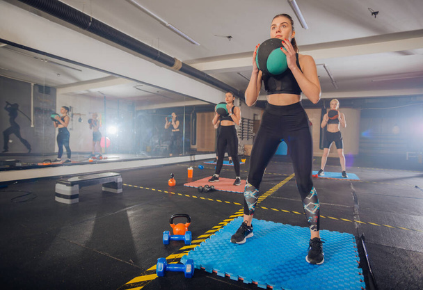 Fitnessgruppe mit vier attraktiven Frauen macht Übungen und Kniebeugen mit Medizinball - Foto, Bild