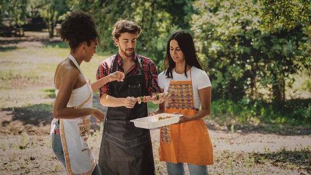 Skupina tří mladých lidí se baví o víkendu vaření špejle na grilu na venkově - Fotografie, Obrázek