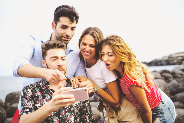 csoport a fiatalok nyaralás szórakozás tengerparton nézi a szociális hálózati tartalmak okostelefon képernyőn - Gen z emberek szórakozás hétvégén - Fotó, kép