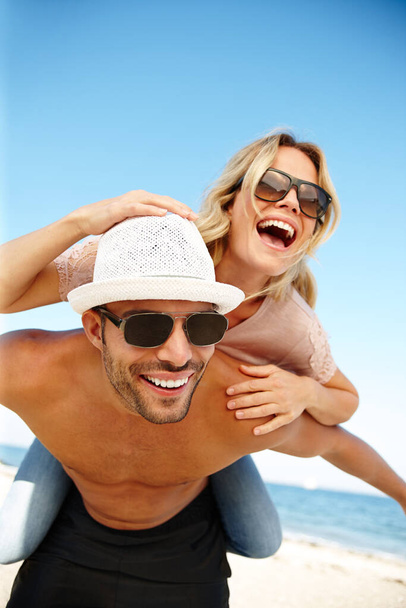 Lustige Urlaubstage. Aufnahme eines lächelnden jungen Mannes, der seiner lachenden Freundin ein Huckepack an einem sonnigen Strand reicht. - Foto, Bild