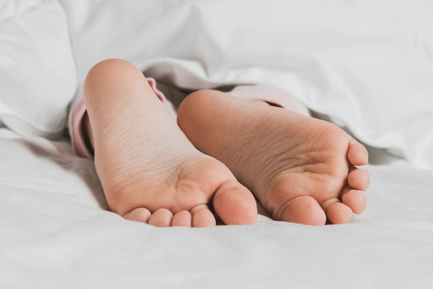 Childs legs are covered with white bed linen. The warmth of home comfort - Φωτογραφία, εικόνα