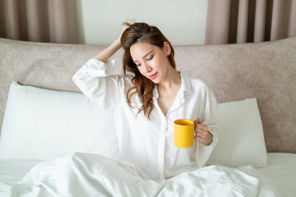 portrait beautiful Asian woman wake up and holding coffee cup or mug on bed in the morning - Foto, afbeelding