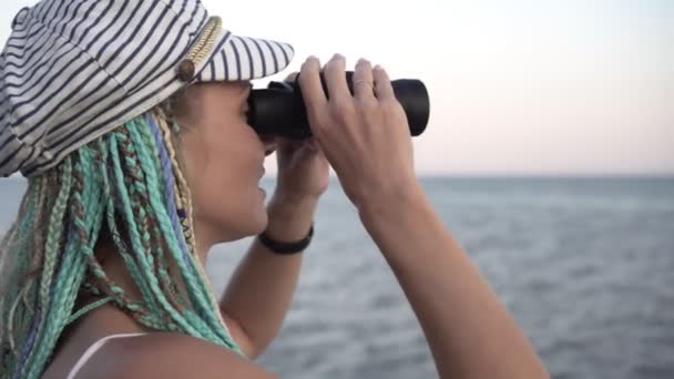 Una mujer mira a través de binoculares hacia el mar. Una persona se para en la orilla y mira a través de los prismáticos. - Metraje, vídeo