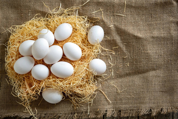 Huevos de pollo blanco en el nido de paja en tela de arpillera - Foto, Imagen