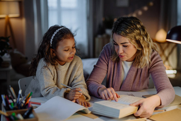 Little girl doing homework with her mother in evening at home. - Foto, Imagen