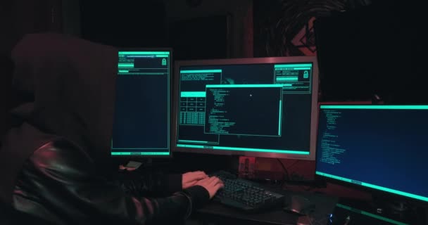Hacker in een kap zit voor computerschermen en hacks databases - Video