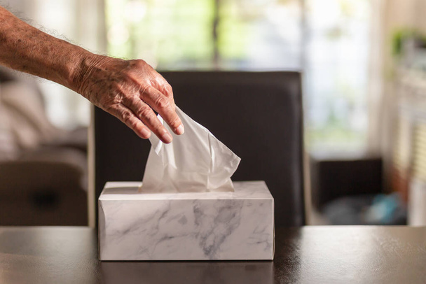 Senior man hand picking up tissue paper from tissue box on dinner table. - Foto, afbeelding