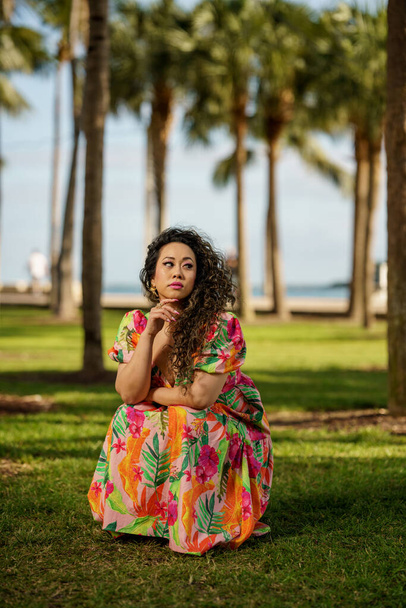Woman in a floral pattern dress squatting in the park - Photo, Image