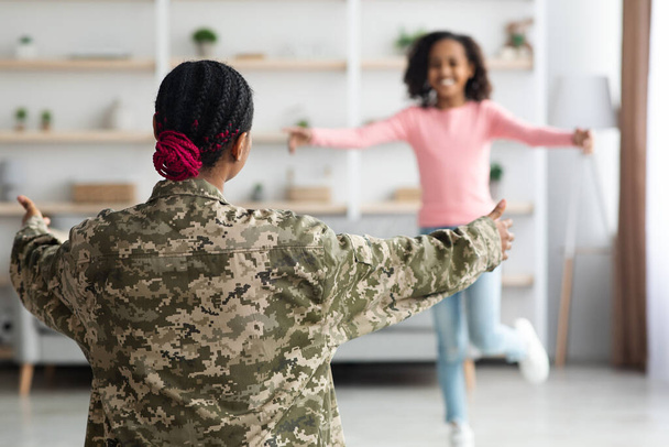 Αγνώριστο μαύρο κορίτσι τρέχει προς τη γυναίκα με στρατιωτική στολή - Φωτογραφία, εικόνα
