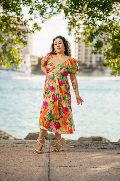 美しい女性は水によって花のドレスに身を包んだ。彼女はマイアミビーチのシーンにいる - 写真・画像