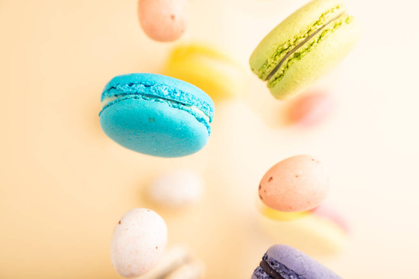 Multicolored flying macaroons and chocolate eggs frozen in the air on blurred beige background. top view, flat lay, close up. Breakfast, morning, concept. - Foto, immagini