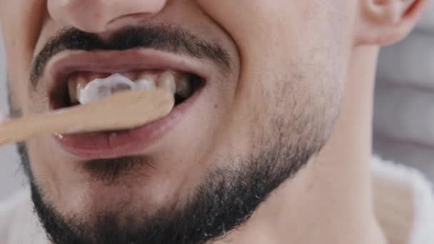 Ekstremalne zbliżenie nierozpoznawalny brodaty człowiek mycie zębów z białej pasty środek wybielający z drewnianą szczoteczką do zębów czyste ustne zdrowie zębów w domu łazienka rano rutynowe codzienne higieny koncepcji opieki - Materiał filmowy, wideo