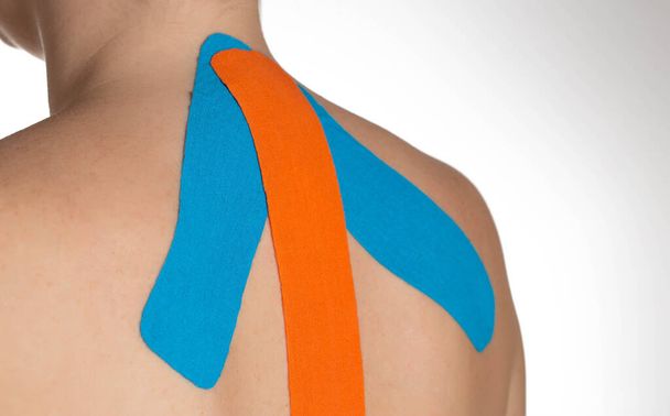 Colocando el cuello y los hombros de la chica con cinta cinesiológica azul y naranja. Medicina alternativa, entrenamiento muscular y de ligamentos, primer plano - Foto, imagen