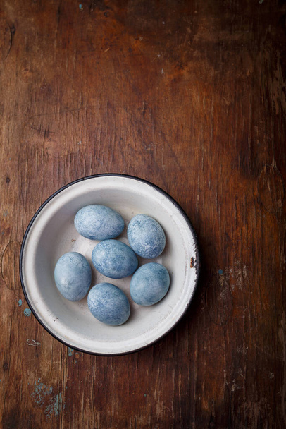 Easter eggs painted blue in white bowl on brown wooden background. Vertical shot, top view on countryside table. - Foto, Bild
