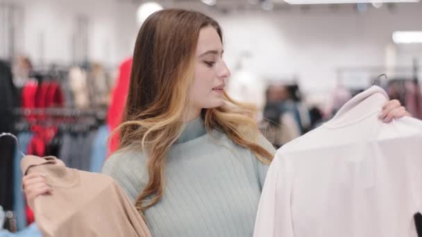 Kavkazský zamyšlený přemýšlivý stylový dívka žena klient kupující zákazník stojí v obchodě s oblečením nákupní obchod obtížná volba mezi dvěma módní svetry jumpery myšlení pocit pochybnosti  - Záběry, video