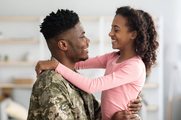 Πλευρική άποψη του μαύρου πατέρα με στρατιωτική στολή αγκαλιάζει το παιδί - Φωτογραφία, εικόνα
