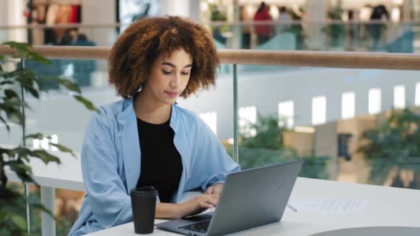 Африканська студентка-американка Міленіальна бізнес-жінка менеджер користувача жінка сидить за столом в кафе і п'є чай для кави, працюючи з ноутбуком надруковуючи онлайн-навчання вивчення мережі wifi - Кадри, відео