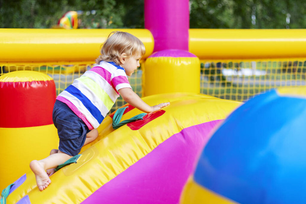 Szczęśliwe dzieci bawiące się na kolorowym nadmuchiwanym placu zabaw. Dzieci bawią się i jeździć na świeżym powietrzu plac zabaw. - Zdjęcie, obraz