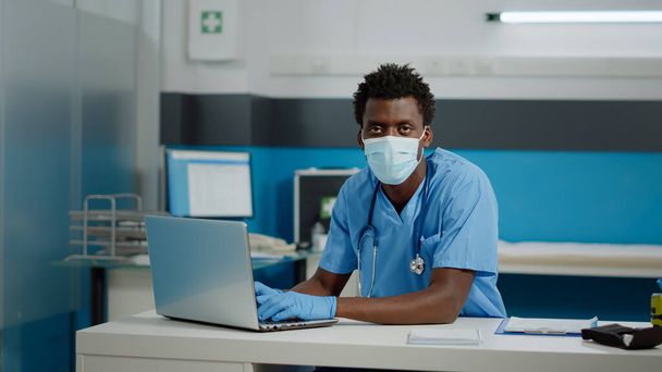 Ιατρική βοηθός πληκτρολογώντας στο πληκτρολόγιο laptop κάθεται στο γραφείο - Φωτογραφία, εικόνα