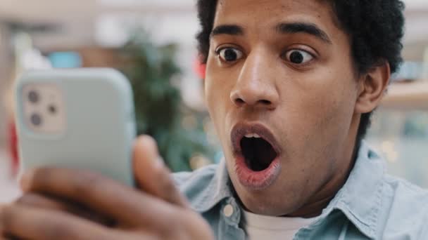 Close-up portrait shocked African American millennial man open mouth in shock looking at smartphone screen feel astonishment scare with bad unexpected news failure fired from work guy looks at phone - Footage, Video