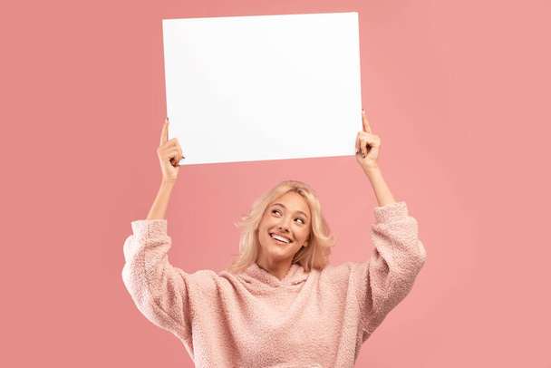 Mosolygó hölgy kezében üres tábla reklám vagy szöveg a feje fölött, álló rózsaszín háttér, másolás hely - Fotó, kép