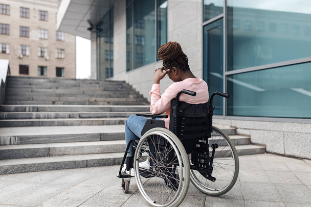 Tekerlekli sandalyeye uygun olmayan genç, mutsuz siyahi kadın, rampasız eve gidemiyor, kopyalama alanı olmadan. - Fotoğraf, Görsel