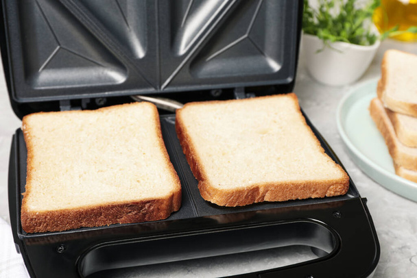 Modern sandwich maker with bread slices on light grey table, closeup - Foto, Imagem