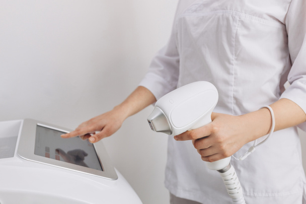 A woman tunes a laser hair removal machine. Girl holding a working part of the epilator in her hands in a modern beauty salon. Underarm Laser Hair Removal concept - Φωτογραφία, εικόνα