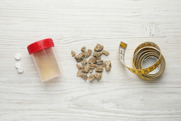 Kidney stones, jar of urine and measuring tape on white wooden table, flat lay - Foto, imagen