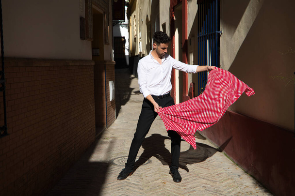 Flamenco- und Zigeunermann in schwarz-weißem Hemd tanzt mit einem gepunkteten Taschentuch in der Hand in einer Gasse in den Straßen einer Mittelmeerstadt. Flamenco-Kulturerbe der Menschheit - Foto, Bild