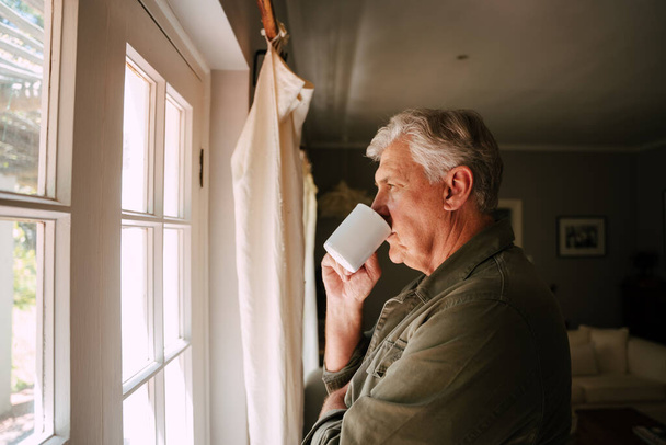 Blanke oudere man drinkt koffie en kijkt uit het raam. - Foto, afbeelding