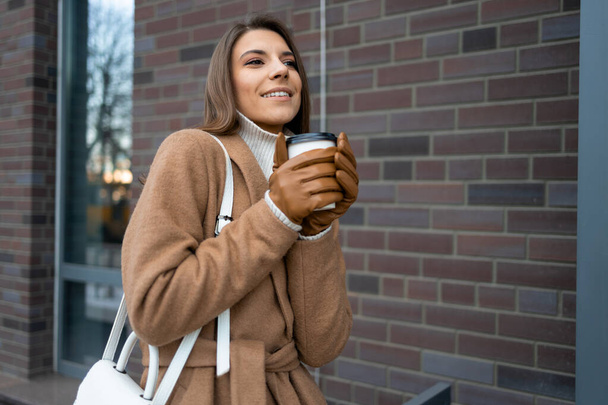Veselá žena drží šálek horké kávy v rukou v chladném období na ulici - Fotografie, Obrázek