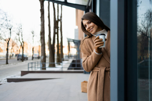 Красивая женщина в коричневом пальто с чашкой кофе на открытом воздухе - Фото, изображение