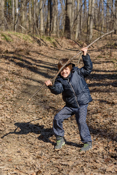 Ένα αγόρι παίζει με ένα ξύλινο ραβδί στο δάσος - Φωτογραφία, εικόνα