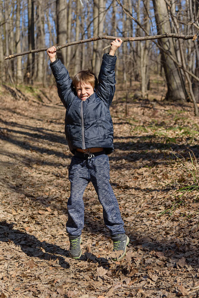 Un niño está jugando con un palo de madera en el bosque - Foto, Imagen