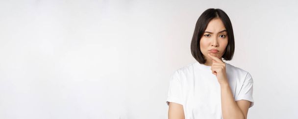 Femme asiatique réfléchie regardant de côté, réfléchissant, faisant des suppositions, pensant ou choisissant smth, debout sur fond blanc - Photo, image