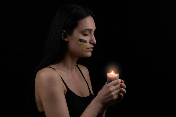 Patriotic ukrainian woman with burning candle are praying for Ukraine. Dark background. Space for text - Foto, Imagen