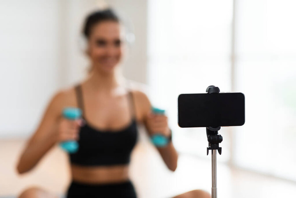 Mujer joven haciendo ejercicio con mancuernas delante del teléfono celular - Foto, Imagen