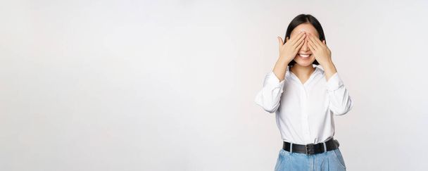 Image of young asian woman close her eyes and smiles, waits for surprise, anticipates, stands over white background - Photo, Image