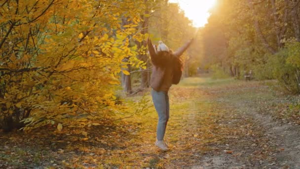 Genç, neşeli, neşeli İspanyol kız güz parkında yürüyor, zıplıyor, doğanın tadını çıkarıyor, güneşli sıcak bir günde güzel havanın tadını çıkarıyor. - Video, Çekim