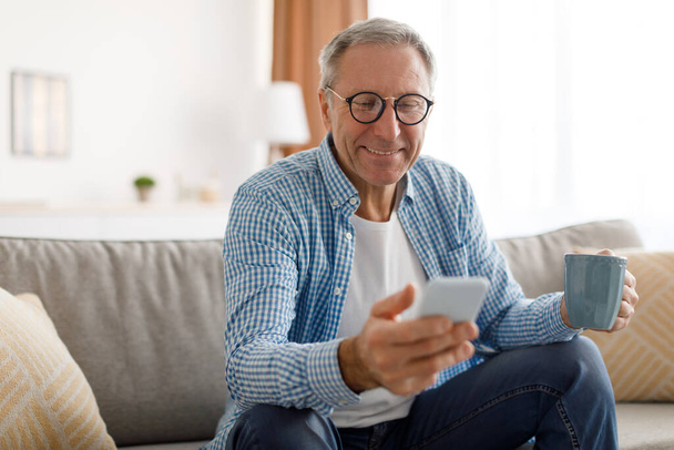 Portrait of smiling mature man using smartphone at home - Photo, Image