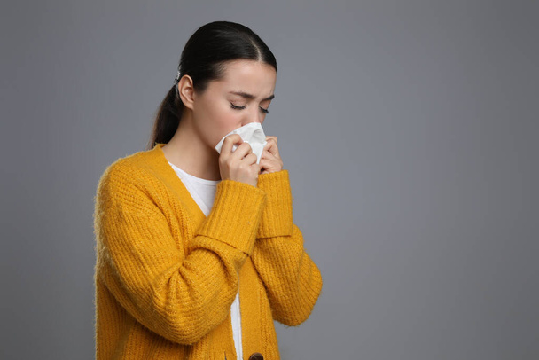 Young woman blowing nose in tissue on grey background, space for text. Cold symptoms - Foto, immagini